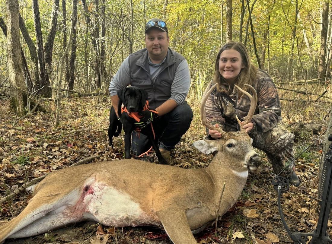 Hunter and a young woman kneeling with a tracking dog behind a recovered buck