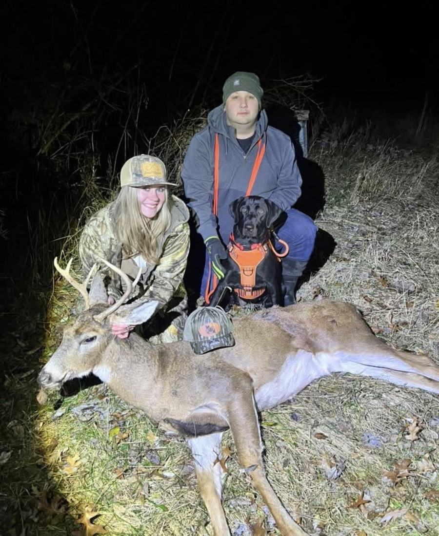 Young hunter and handler with a tracking dog and a recovered buck at night