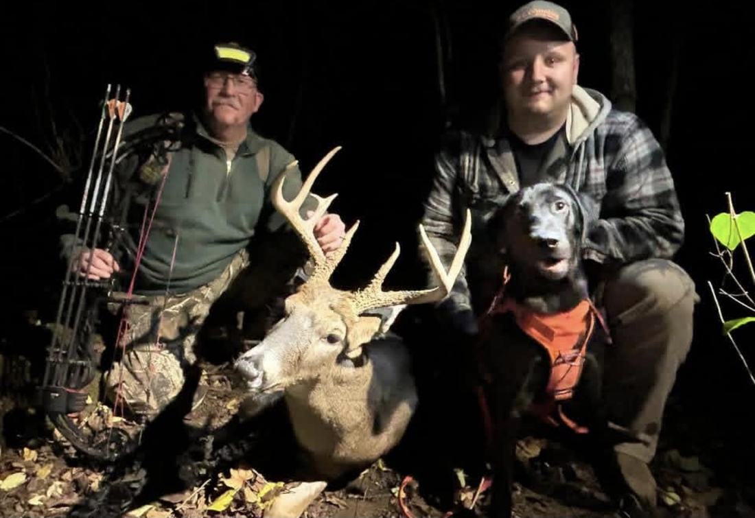 Bowhunter and handler with a large buck and a tracking dog at night